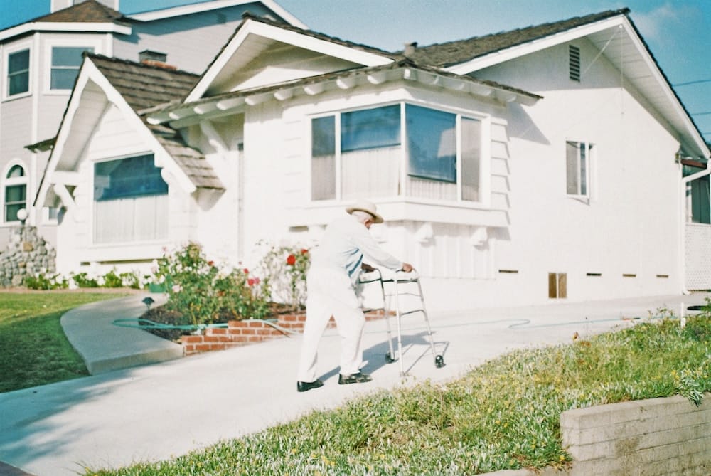 Image of an older man walking up a driveway using a walker.