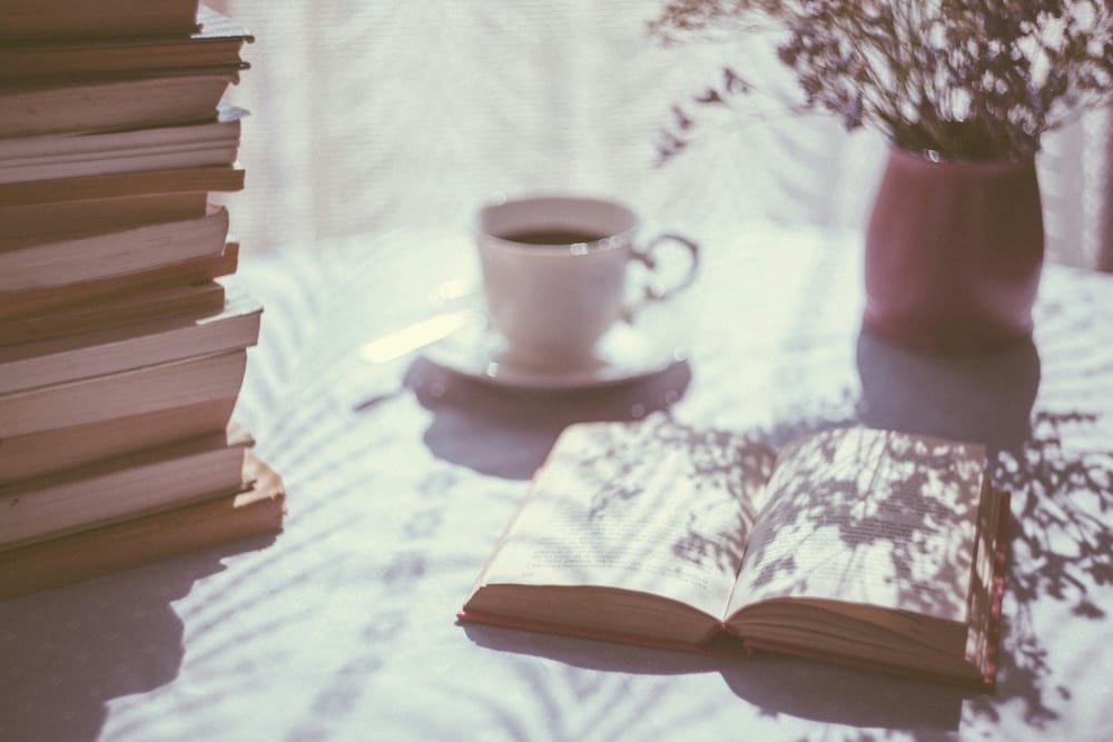 Image of an open book next to a white ceramic teacup, a stack of books, and a plant.