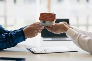 Photo of a model house being transferred between people