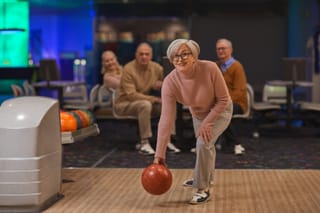 Image of a senior woman bowling with friends watching