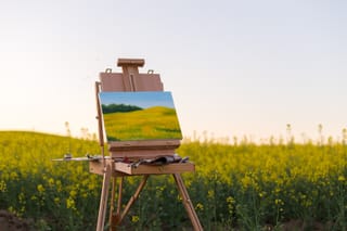 Picture of an art board and easel in a field of flowers with a completed landscape painting