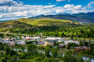 Picture of downtown Missoula Montana with mountains in the background and a river in the foreground 