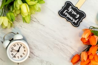 Image of a clock with flowers and a sign that reads spring forward