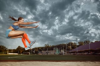 Photo of a woman participating in the long jump at a stadium 