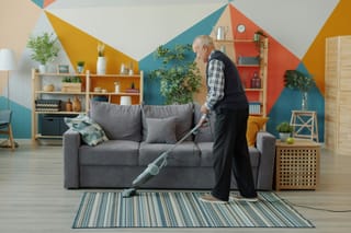 Image of older man vacuuming a living room carpet.