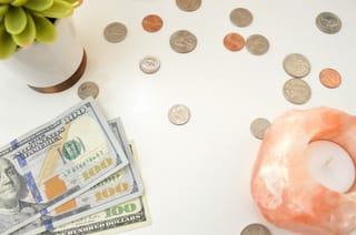 Image of US bills and coins on a table with a plant and a candle