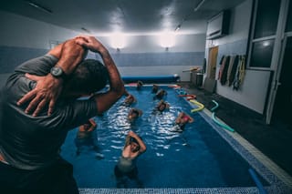 Image of an instructor leading a group of people stretching in an indoor pool