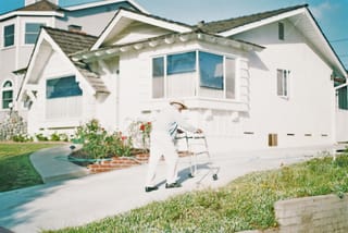 Image of an older man walking up a driveway using a walker.