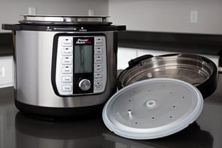 A stainless-steel Power Quick Pot pressure cooker on a dark kitchen counter, with its lid upside down beside it and a translucent round disc in front.