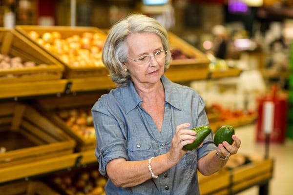 Photo of a senior woman at grocery store looking at avocados