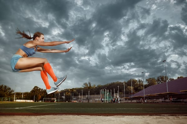 Photo of a woman participating in the long jump at a stadium 
