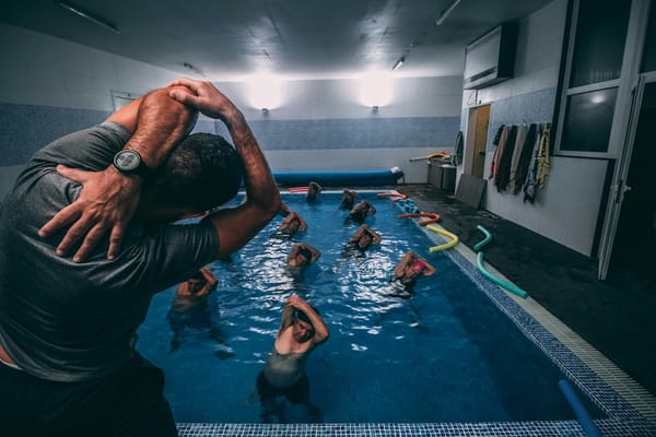 Image of an instructor leading a group of people stretching in an indoor pool