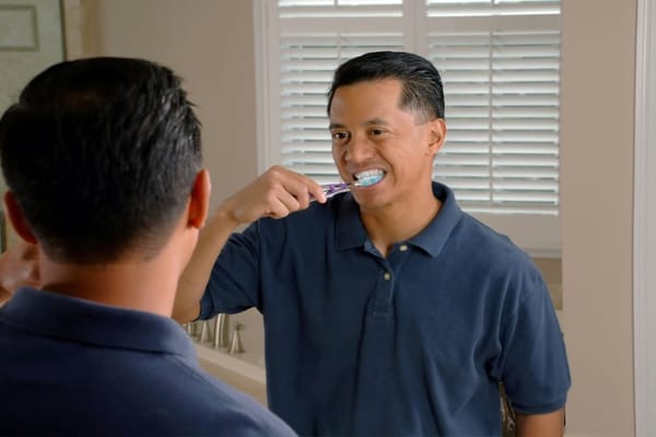 Image of a man brushing his teeth while looking in a mirror.