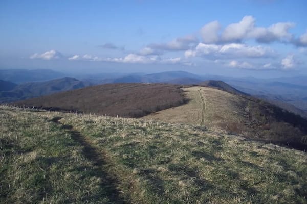Image of a trail on top of mountains with clouds in the sky.