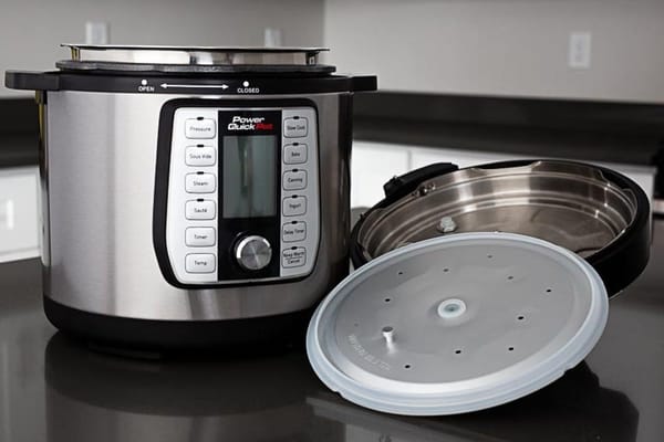 A stainless-steel Power Quick Pot pressure cooker on a dark kitchen counter, with its lid upside down beside it and a translucent round disc in front.